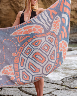 Person holding a large towel with a turtle pattern by a body of water.