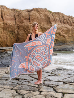 Woman holding a patterned towel by a rocky beach with cliffs in the background