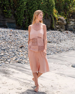 Woman in a pink dress standing on a pebbly beach with greenery in the background
