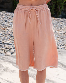 Person wearing peach-colored shorts with a drawstring on a pebbly beach.