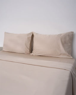Beige bed sheets and pillowcases on a bed with a plain background