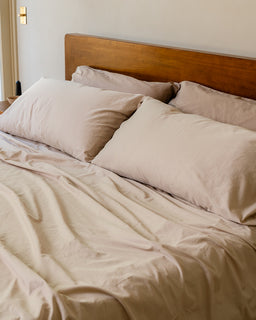Neatly made bed with beige bedding and pillows in a bedroom setting.