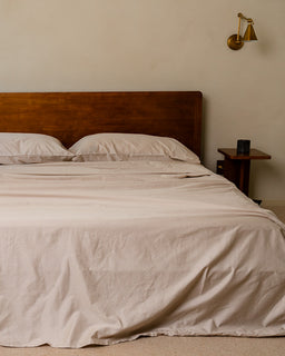 Bedroom with a wooden headboard and beige bedding, featuring a wall sconce.