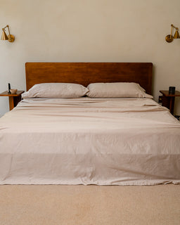 Bed with beige bedding and wooden headboard in a room with wall sconces.