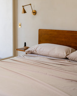 Bedroom with wooden headboard, beige bedding, and wall-mounted lamps.