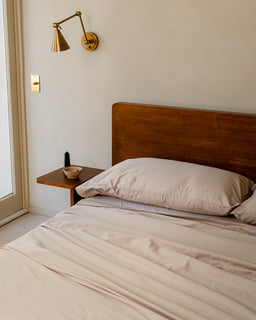 Bedroom with wooden headboard, beige bedding, and wall-mounted lamp.