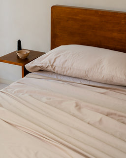 Beige bedding on a bed with a wooden headboard and side table.