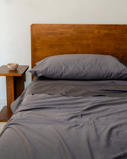 Bed with gray bedding and wooden headboard against a white wall