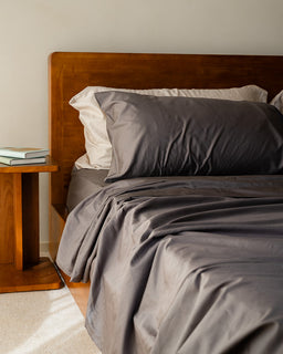 Bed with gray bedding and wooden headboard in a bedroom setting