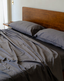 Bed with gray bedding and pillows against a wooden headboard.