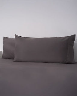 Two dark gray pillows on a matching gray bedspread against a light gray background