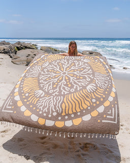 Person holding a large decorative beach towel on a rocky beach with ocean in the background