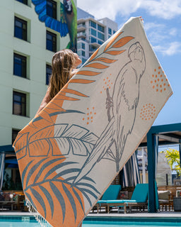 Person holding a decorative towel with a parrot design by a poolside.