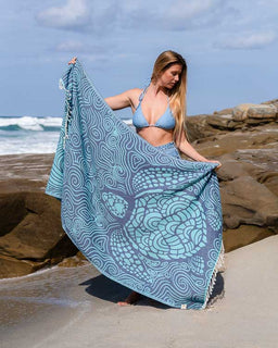 Woman on a beach holding a blue and gray patterned towel