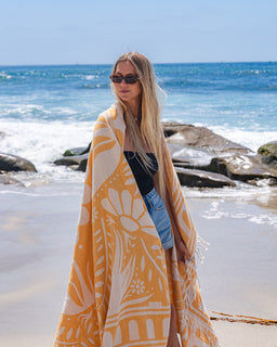 Woman wrapped in a yellow patterned towel on a beach with ocean in the background