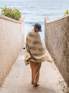 Person wrapped in a pineapple-patterned blanket walking along a coastal path.