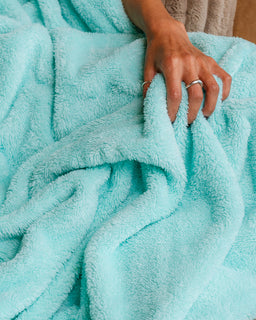 A close-up of a person's hand resting on a soft, plush aqua blue blanket, showing the texture of the fabric.