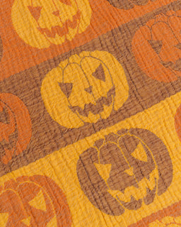 A close-up of a Halloween-themed fabric featuring a repeating pattern of orange and brown jack-o'-lantern pumpkins on a textured woven background.