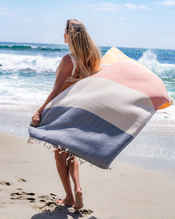 Woman holding a striped beach towel on a sandy beach with ocean waves in the background