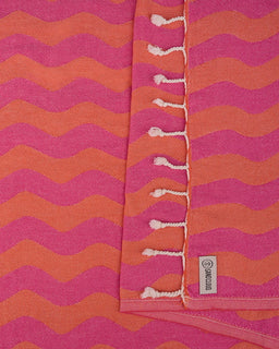 Pink and orange striped towel with tassels and a brand label.