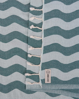Textile with wavy pattern and tassels, featuring a brand label.