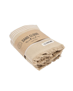 A folded beige cotton towel with white stripes and fringed edges, wrapped in a kraft paper band printed with 'SAND CLOUD' and a small white brand tag, on a plain white background.