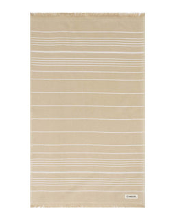 A beige cotton bath towel with thin white horizontal stripes and fringed edges, featuring a small white brand label in the bottom right corner.