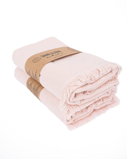 A folded light pink cotton bath towels with fringed edges, wrapped in a brown paper band 