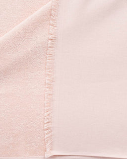 A close-up of a pale blush pink fabric with a soft, textured weave and a fringed edge.
