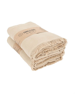 A folded beige cotton blanket with fringed edges, wrapped in a brown paper band 