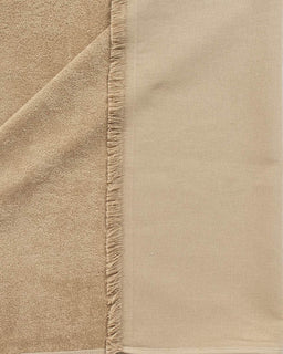 A close-up of a beige textile product, showing two textures: a plush terry side and a smoother woven side, finished with a fringed edge.