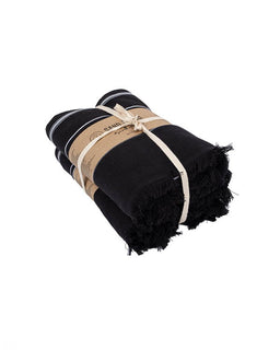 A folded black bath towel with white stripes and fringed edges, wrapped in a kraft paper band tied with a cream ribbon, on a white background.