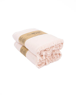 Two folded pale pink cotton towels with fringed edges, wrapped in a brown paper band, on a white background.