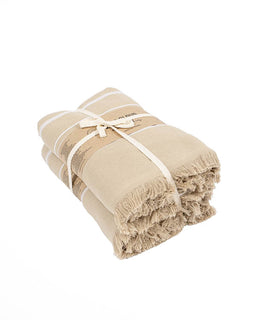 A folded beige cotton bath towel with fringed edges, tied with a cream-colored ribbon, shown on a solid white background.