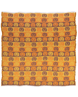 A rectangular woven blanket with fringed edges, featuring a repeating pattern of carved jack-o'-lantern pumpkins in orange, yellow, and brown on a warm orange background.