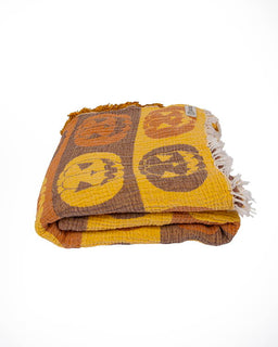 A folded woven throw blanket featuring a yellow and brown pumpkin pattern, with white fringe on one end, photographed on a clean white background.