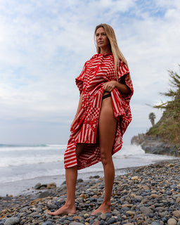 Woman wearing a red and white patterned dress on a rocky beach with ocean and sky in the background