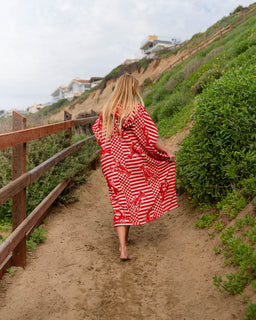 Person walking on a path wearing a red and white patterned poncho with houses and greenery in the background.