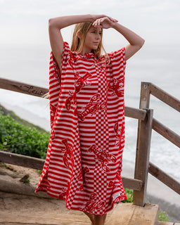 Woman wearing a red and white striped poncho with lobster pattern by a wooden railing.