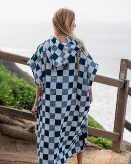 Person wearing a blue and white checkered poncho standing on a wooden deck with a scenic background.