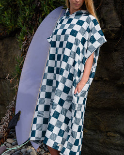 Person wearing a blue and white checkered poncho with a surfboard in the background.