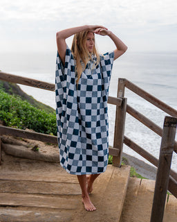 Person wearing a blue and white checkered towel by a wooden railing with a scenic background.