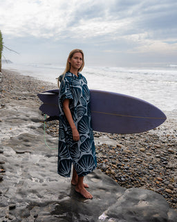 Woman holding a surfboard on a rocky beach with ocean and sky in the background