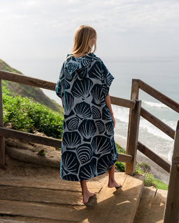 Woman wearing a blue and white patterned dress standing on wooden steps overlooking a coastal view.