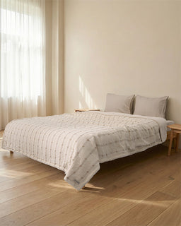 Bedroom with a bed covered in a textured white blanket and light gray pillows.