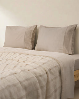 Beige bedding set with pillows on a bed against a plain wall.