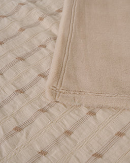 Close-up of a beige quilt with diamond pattern and folded edge