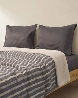 Bed with gray striped bedding and pillows against a beige wall