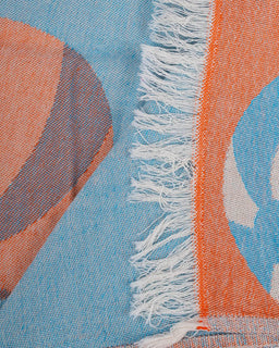 Close-up of a fabric with blue, orange, and white patterns and fringes.