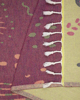 Close up of a maroon beach towel with a marine life design, including jellyfish and sea anemones, with twisted tassels at the bottom.